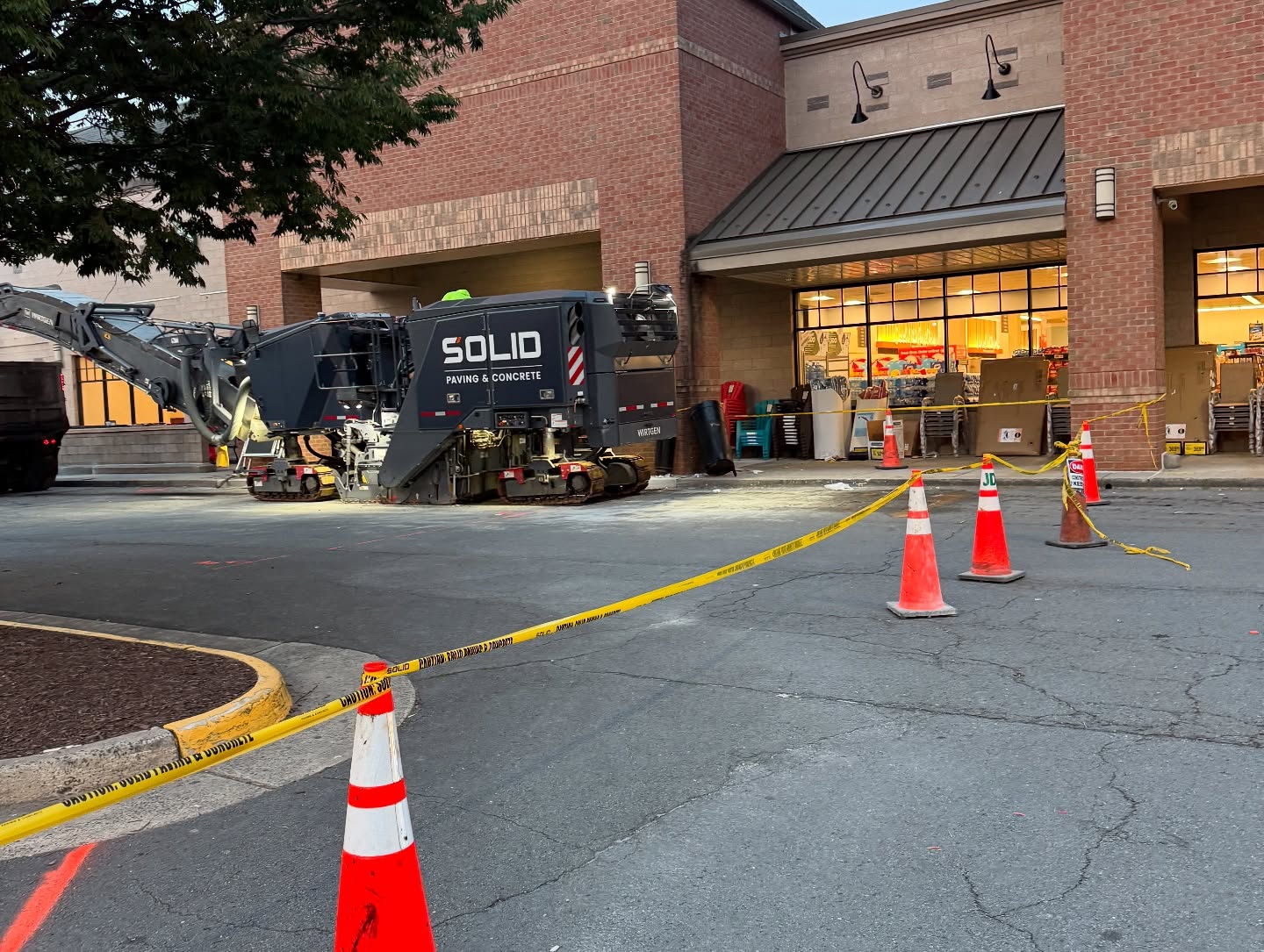 A construction vehicle labeled Solid Paving & Concrete is parked outside a store, with caution tape and cones blocking off the area.