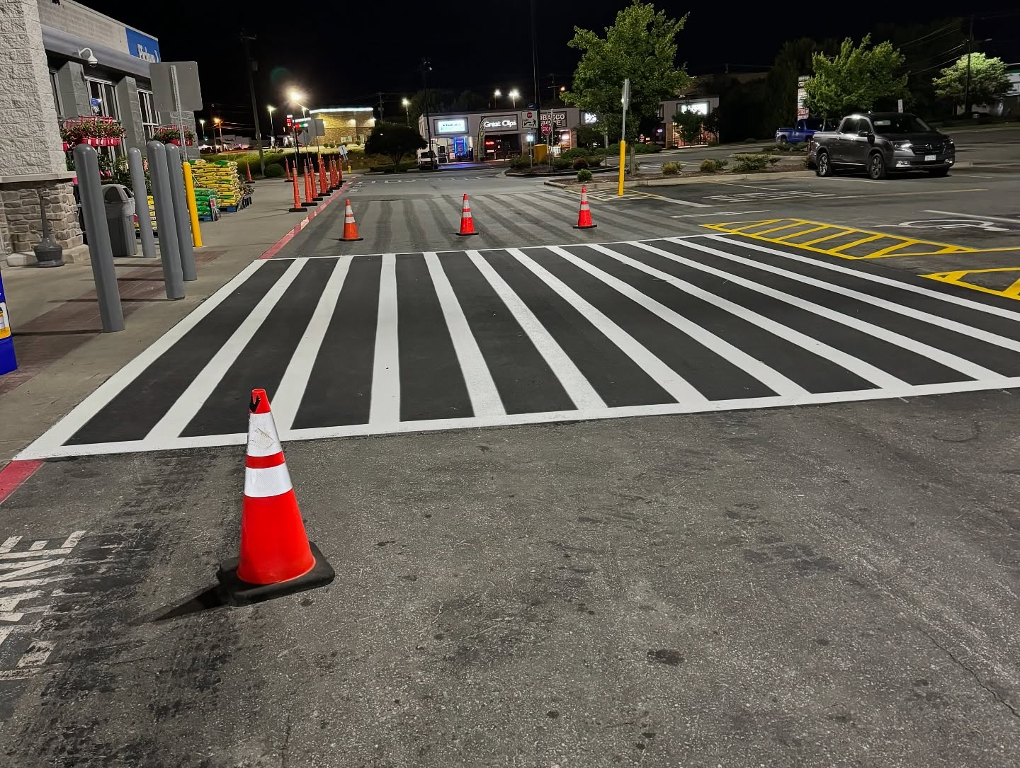 A newly painted crosswalk with orange traffic cones blocks access in a parking lot at night, showcasing fresh roadway thermoplastic lines.